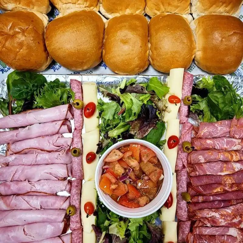 Meat and cheese tray with rolls, lettuce, and a cup of pepper relish